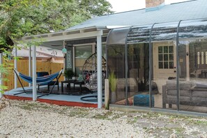 Un patio cubierto con una hamaca, asientos y un cerramiento de vidrio.