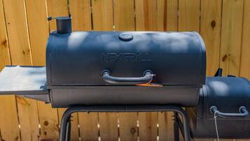 A black NEXGRILL barbecue grill with a handle and a lid, set against a wooden fence background.