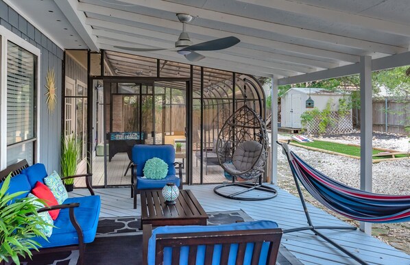 Un patio techado al aire libre con un sofá azul, un sillón colgante y una hamaca.