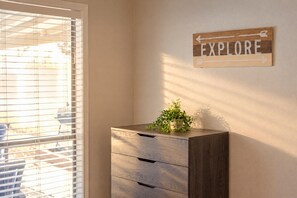 Una habitación con ventana y persianas, un armario de madera con cajones y un cartel en la pared que dice 'EXPLORE'.