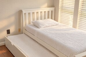 A white bed with a headboard, a single pillow, and a mattress on a wooden floor. - 4BR Family Retreat with Game Room, Sunroom & Huge Backyard (San Antonio)