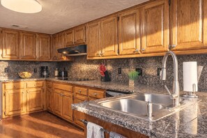 A kitchen with wooden cabinets, granite countertops, a stainless steel sink, and a built-in dishwasher. - 4BR Family Retreat with Game Room, Sunroom & Huge Backyard (San Antonio)