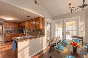 Cocina con armarios de madera, encimera de granito y comedor con vajilla azul.