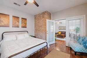 Un dormitorio con cama, pared de ladrillo, puerta y vista a una sala de estar.