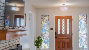 Un pasillo con una puerta de madera, ventanas de vitral, una planta en maceta y un televisor montado.