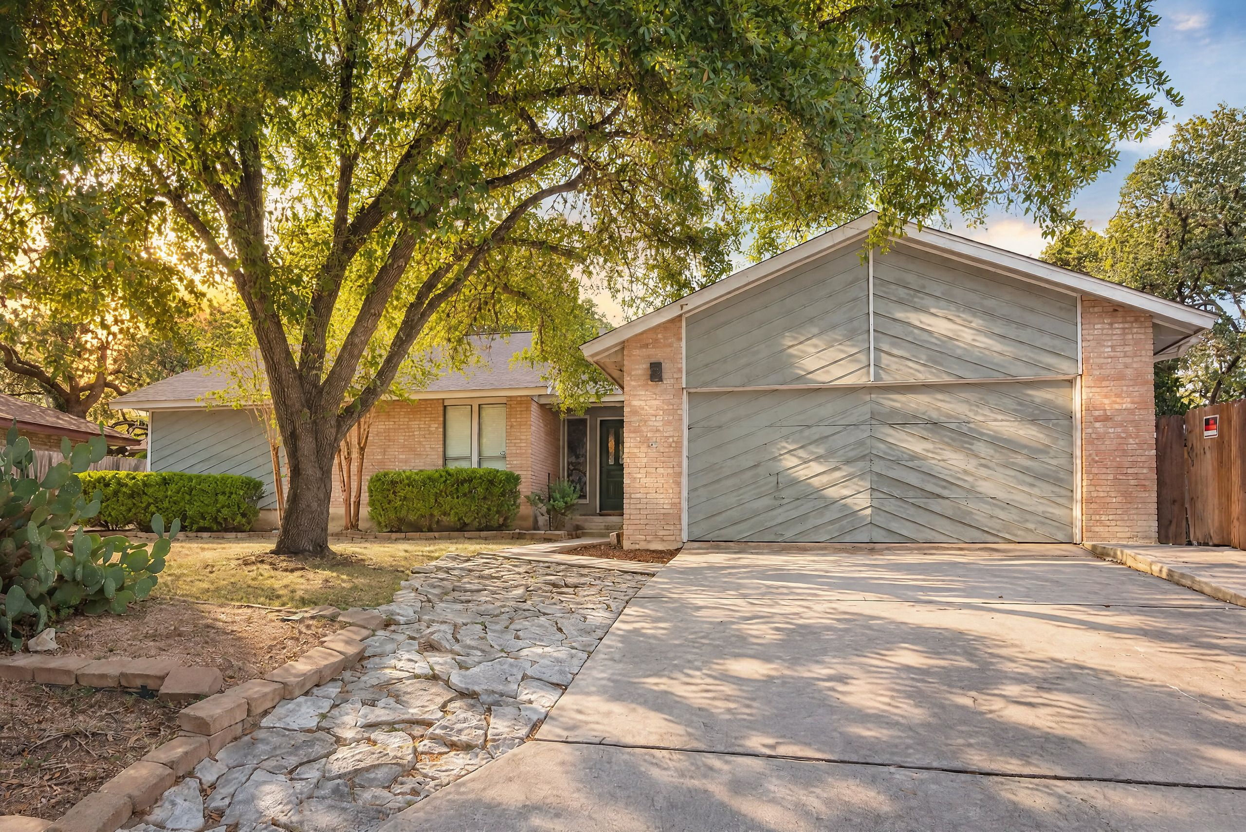 A residential building with a garage, stone pathway, and a tree in the yard.