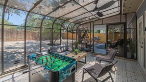 Un espacio al aire libre techado con mesa de fútbol de mesa, asientos y vista al patio trasero.