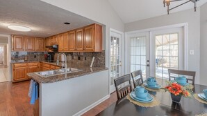 Una cocina con armarios de madera, encimeras de granito y una zona de comedor con vajilla azul.