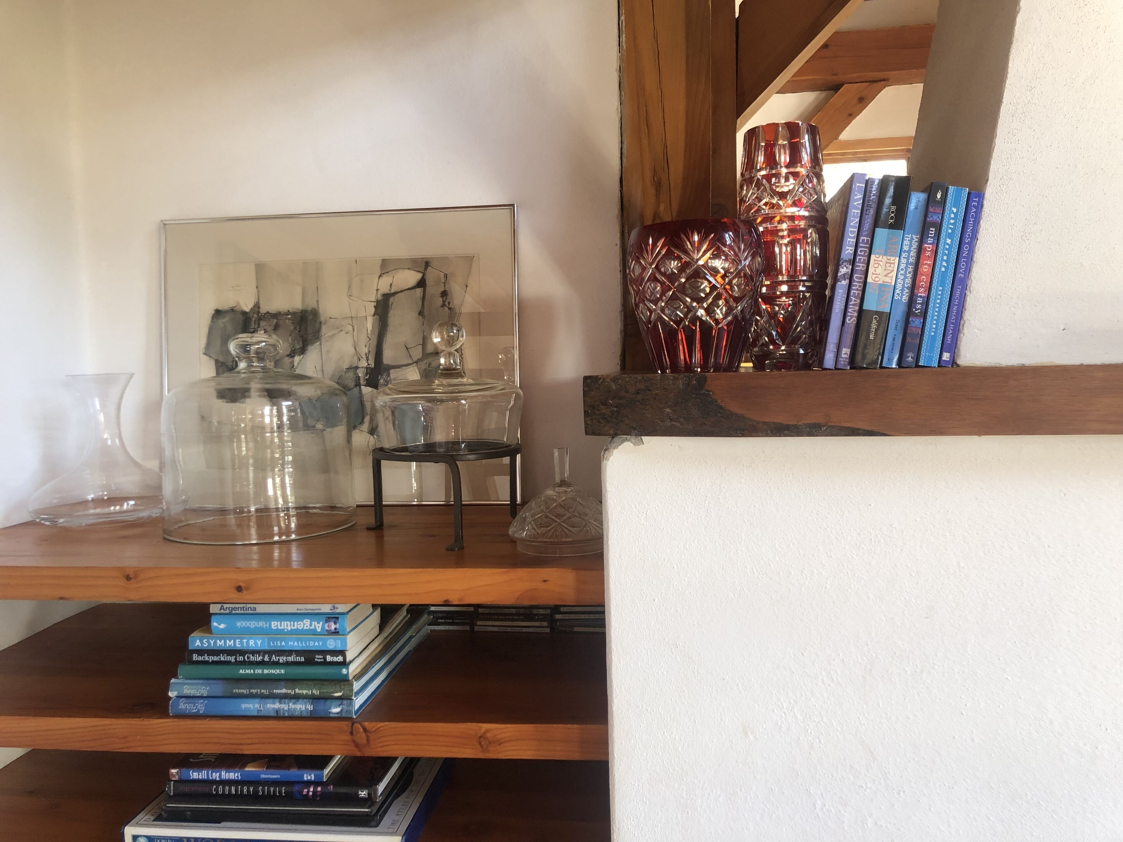 Una estantería de madera con libros, adornos de cristal y un cuadro abstracto enmarcado.