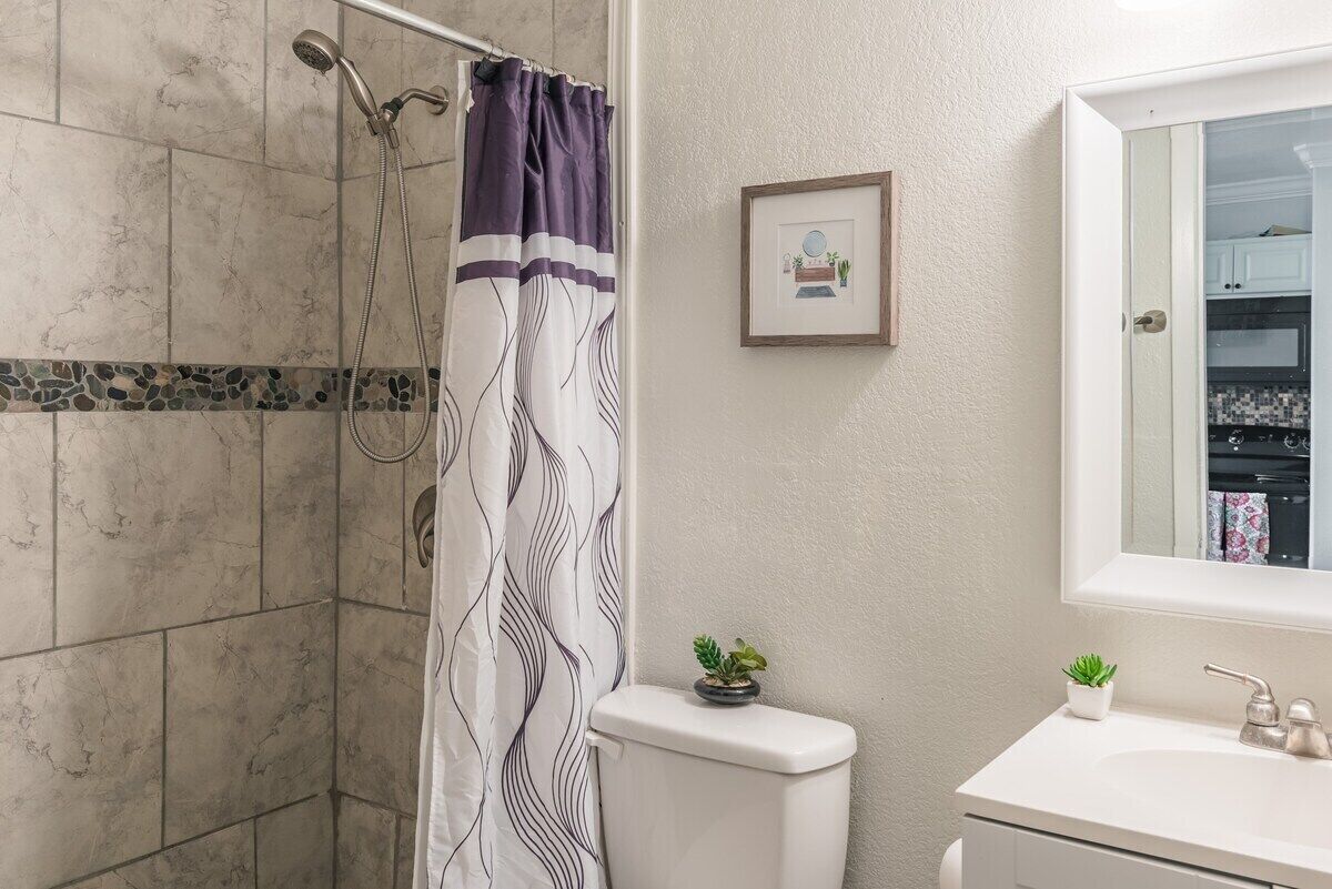 Ein Badezimmer mit Dusche, Toilette, Waschbecken und einem gerahmten Bild an der Wand.