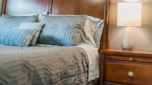 A neatly made bed with patterned bedding and pillows, a wooden nightstand with a lamp, and a drawer.