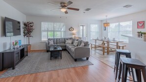 A spacious living room with a sectional sofa, a coffee table, a TV, and a ceiling fan.