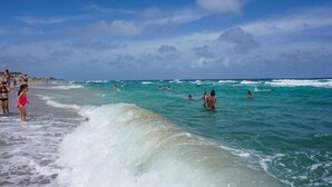 Ein Strand mit badenden und am Ufer entlang gehehenden Personen.