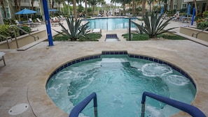 Zona de hidromasaje con piscina al fondo, rodeada de sillas de descanso y palmeras.