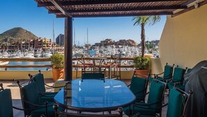 A covered outdoor dining area with a glass table and green chairs, overlooking a marina with boats and buildings. - Stunning Marina views, best location in Cabo! (Cabo San Lucas)