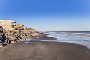 A beach with a rocky shoreline, a building with balconies, and a clear sky. - Historic Beach Cottage - Steps to Beach & Dining (Saint Simons Island)