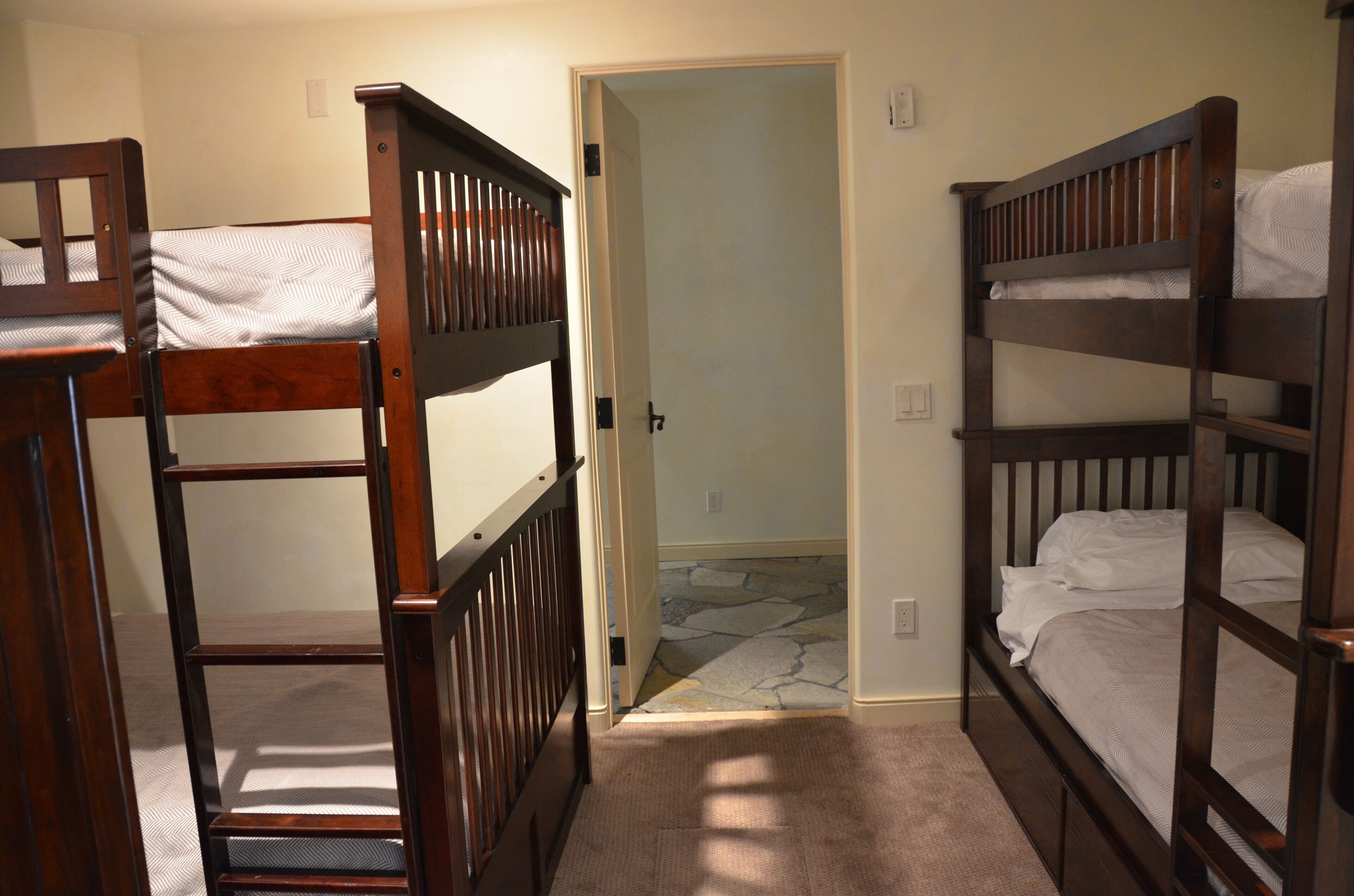 A room with two bunk beds, a carpeted floor, and a door leading to another room.