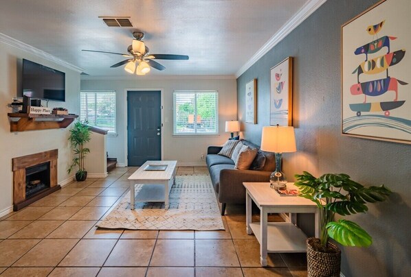 A living room with a fireplace, a ceiling fan, a TV, and a couch.