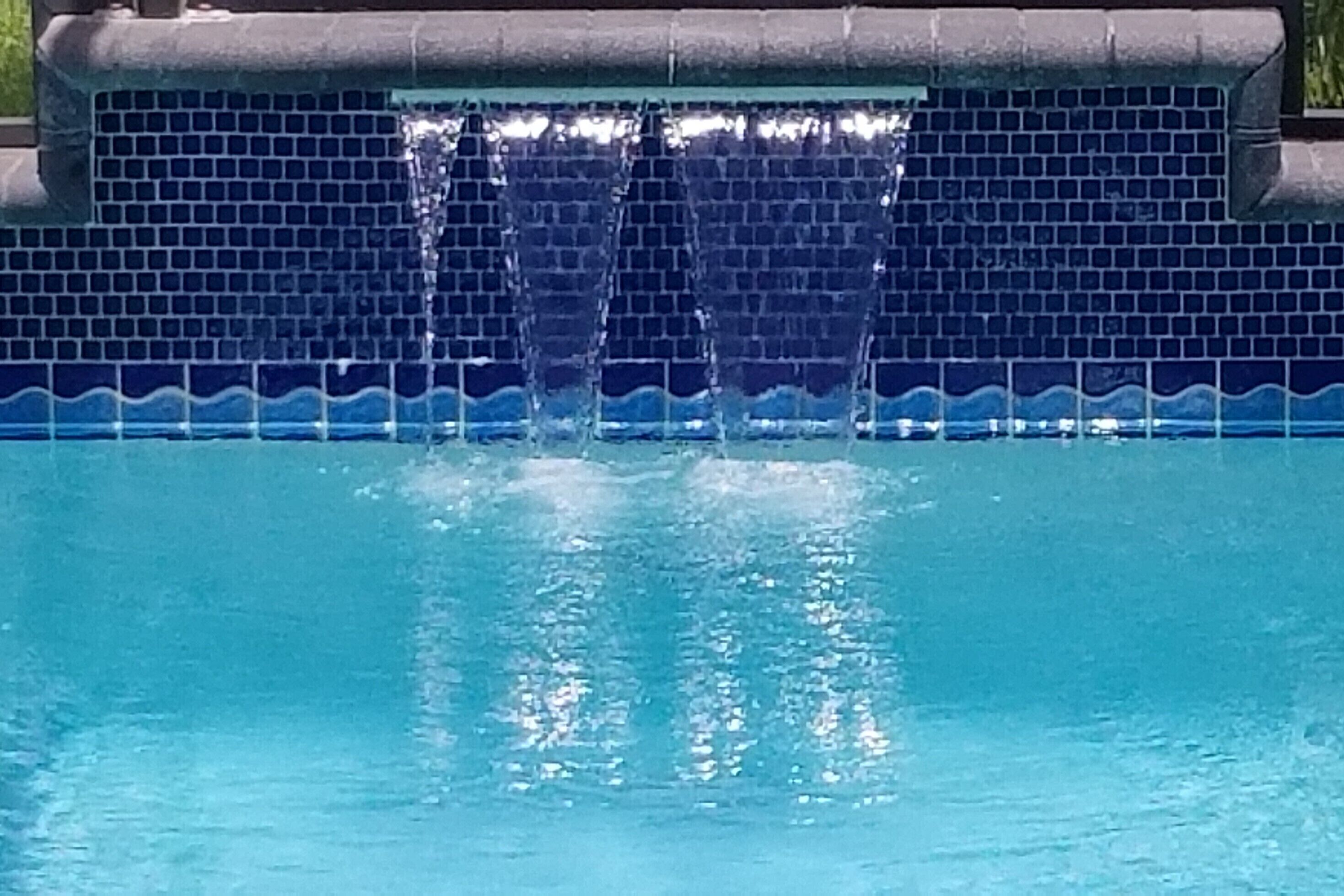A swimming pool with a blue mosaic tile border and a water feature.