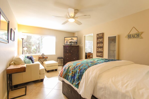 A bedroom with a bed, a desk, a chair, a dresser, a ceiling fan, and a window with blinds.