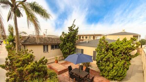 A patio area with a table and chairs, surrounded by potted plants and trees. - "Balboa Beach Escape"  Steps to Beach and Bay A/C + Garage Parking (Newport Beach)