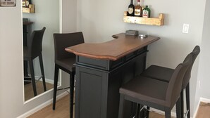 En bardisk med en träbeklädd yta, två barstolar och hyllor med flaskor och glas.