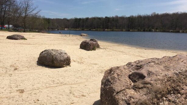 En sandstrand med stora stenar och en lugn sjö.