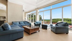 A spacious living area with a large sofa set, a coffee table, and a view of the outdoors through large windows.