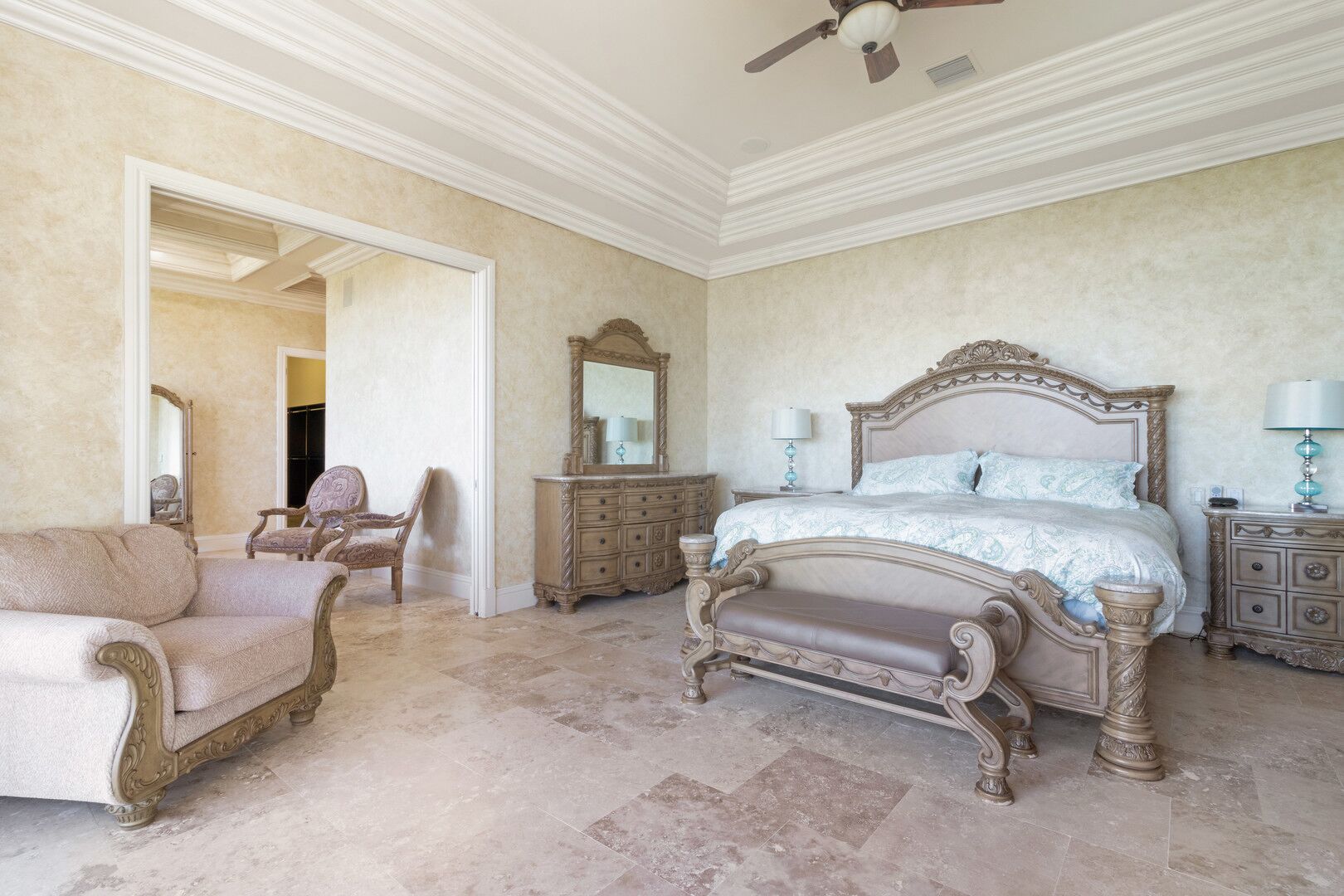 A spacious bedroom with a large bed, a chair, a dresser, and a mirror.