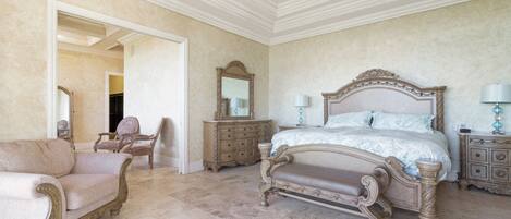 A spacious bedroom with a large bed, a chair, a dresser, and a mirror.