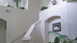 A staircase with a white handrail and carpeted steps, flanked by potted plants and a framed picture on the wall.