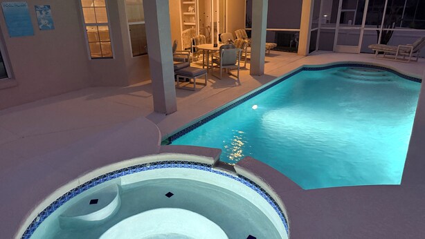 A swimming pool with a hot tub, lounge chairs, and a covered patio area.