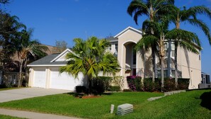A two-story house with a garage, surrounded by well-maintained lawns and palm trees.