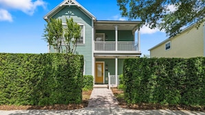A two-story house with a front porch, a small balcony, and a well-maintained hedge.