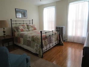 A bedroom with a bed, a nightstand, a lamp, and a radiator. - ' Experience ' The History In Downtown Gettysburg! - 2nd floor (Gettysburg)