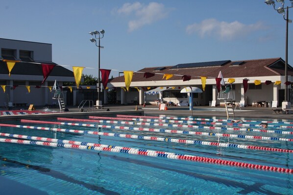 A swimming pool with lane dividers, a lifeguard stand, and a building with a tiled roof.