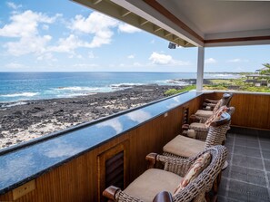 A balcony with wicker chairs overlooking a rocky coastline and ocean.