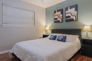 A neatly made bed with a white duvet and two decorative pillows, flanked by two bedside tables with lamps, in a room with a simple, clean design.