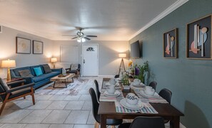 A dining area with a table set for four, a blue sofa, a ceiling fan, and framed artwork on the walls.