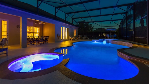 Une piscine intérieure dotée d’un toit en verre, entourée de chaises longues et de tables, ainsi qu’un espace patio avec des chaises et des parasols.