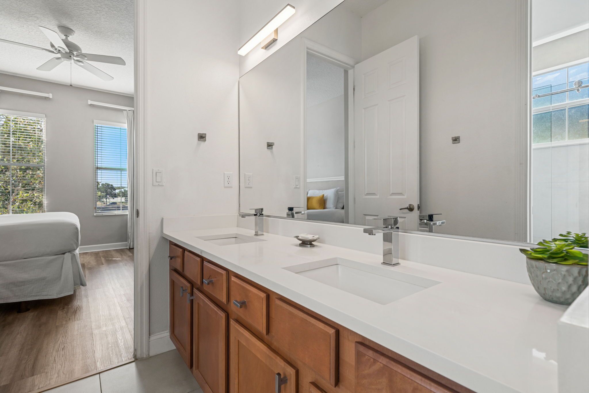 A modern bathroom with a large mirror, two sinks, wooden cabinets, and a ceiling fan.