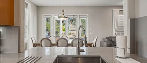 A modern kitchen with a central island, stainless steel sink, and a dining area with chairs and a table.
