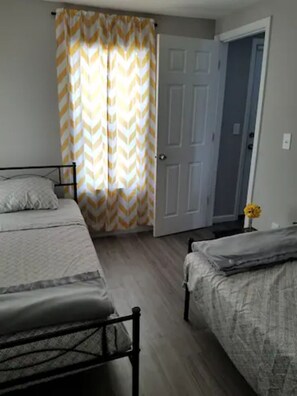 A bedroom with two beds, a door, and a curtain.