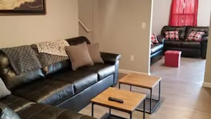A living room with a black leather sofa, a wooden coffee table, and a red ottoman. There is a framed artwork on the wall and a staircase leading to another room. - The Carter's Wildwood Rentals-  Master Suite #3 (Wildwood)
