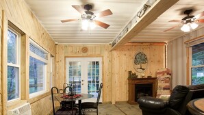A room with wooden walls, a fireplace, a dining table with chairs, and a leather sofa. - Private 50 ft waterfall. Eco-friendly, cozy shipping container cabin (Tracy City)