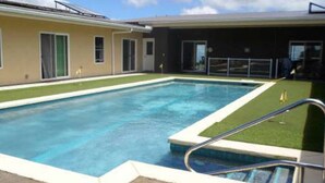 Una piscina rectangular con una escalera de metal, rodeada de césped y un edificio de fachada oscura y amplias ventanas.