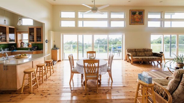 Amplia sala de estar con mesa de comedor, sillas, sofá y área de cocina con armarios de madera y un ventanal grande.