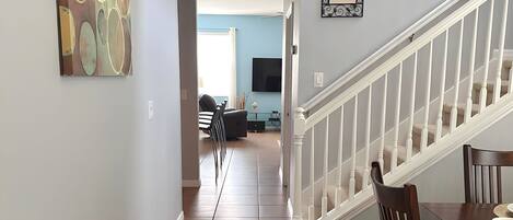 A spacious hallway with a dining area, a staircase, and a living room in the background.
