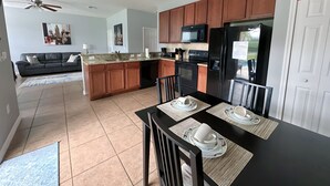 A modern kitchen with a central island, wooden cabinets, a black refrigerator, and a dining area with a black table and chairs. - Amazing 5 bedroom house near Disney (Kissimmee)
