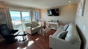 Een woonkamer met een balkon, een flatscreen-tv en een witte bank.